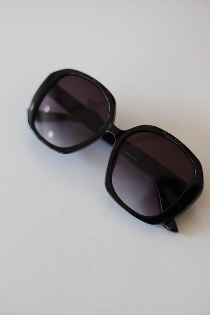 Black oversized square sunglasses with dark gradient lenses, photographed on a plain off-white background.
