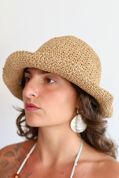A woman wearing a beige woven sun hat with a wide brim, shown in profile against a plain light background.