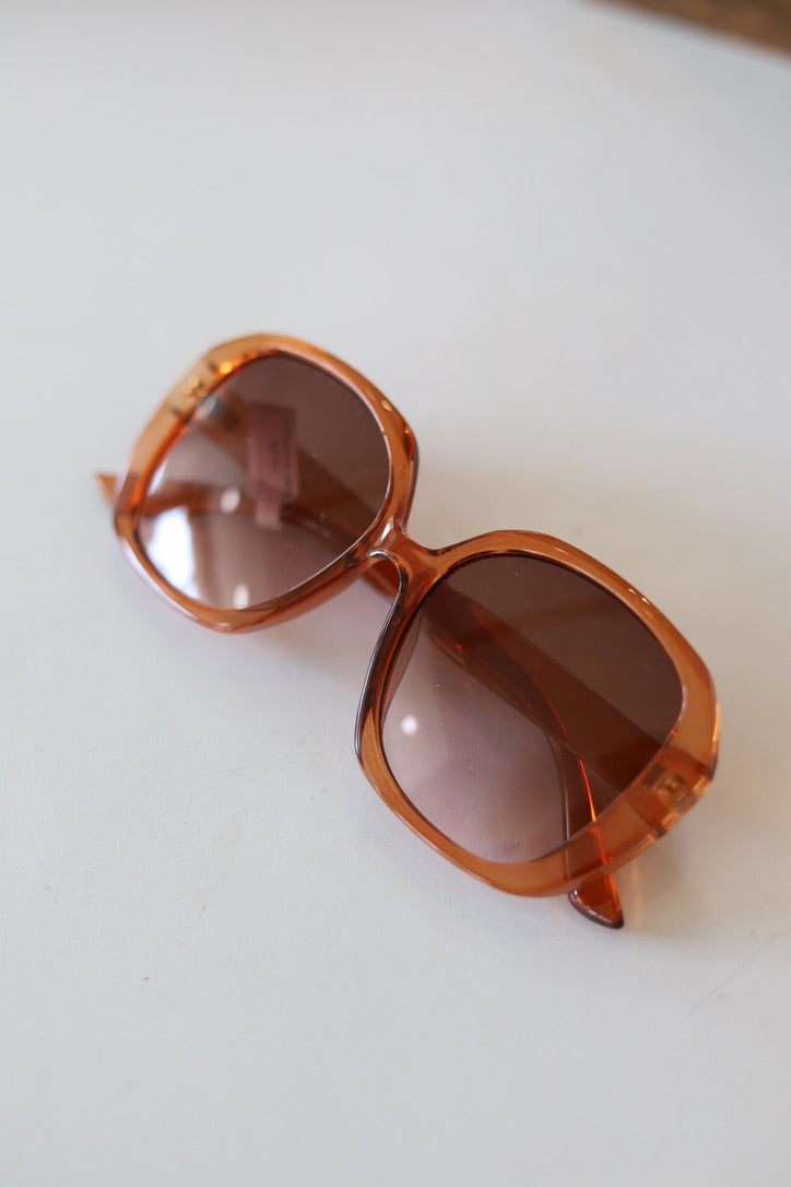 Oversized square sunglasses with a translucent amber-brown frame and tinted brown lenses, resting on a plain white surface.