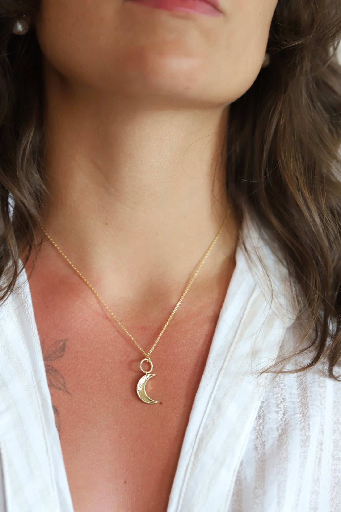 A close-up of a woman wearing a delicate gold chain necklace with a crescent moon pendant, styled with a white top.