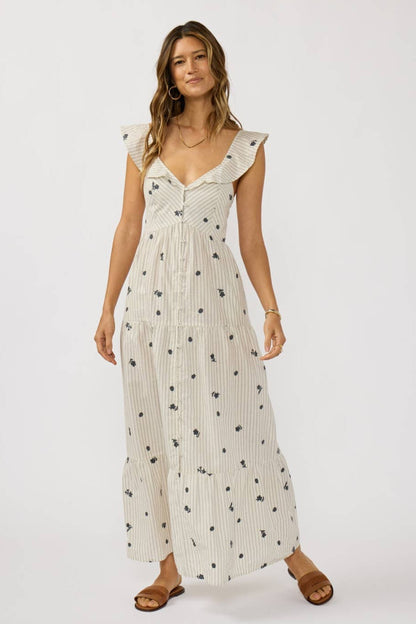 Woman wearing a stripe cream dress with grey floral embroidered patterns on a white background