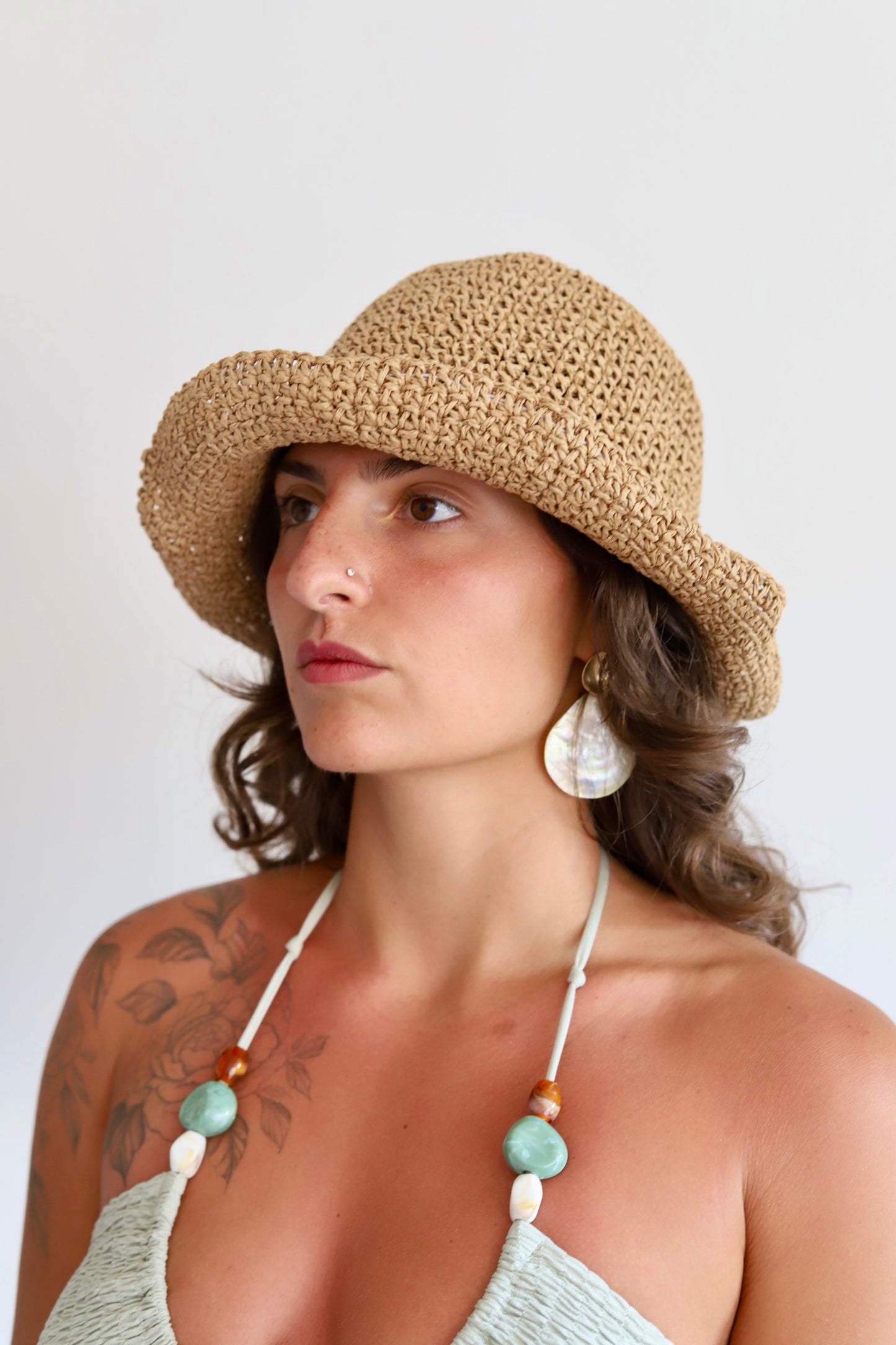 A woman wearing a natural straw sun hat,  and large white shell earrings, shown against a plain light background.