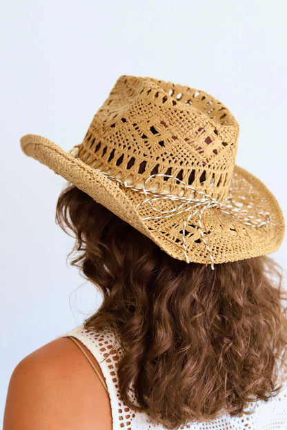 A woman shown from the back wearing a woven straw cowboy hat with a white embroidered bow and brown wavy hair, against a plain light background.