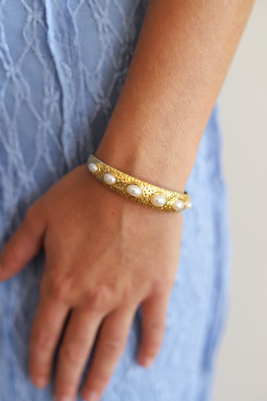 Gold bracelet with a texture. Also features inlaid pearls